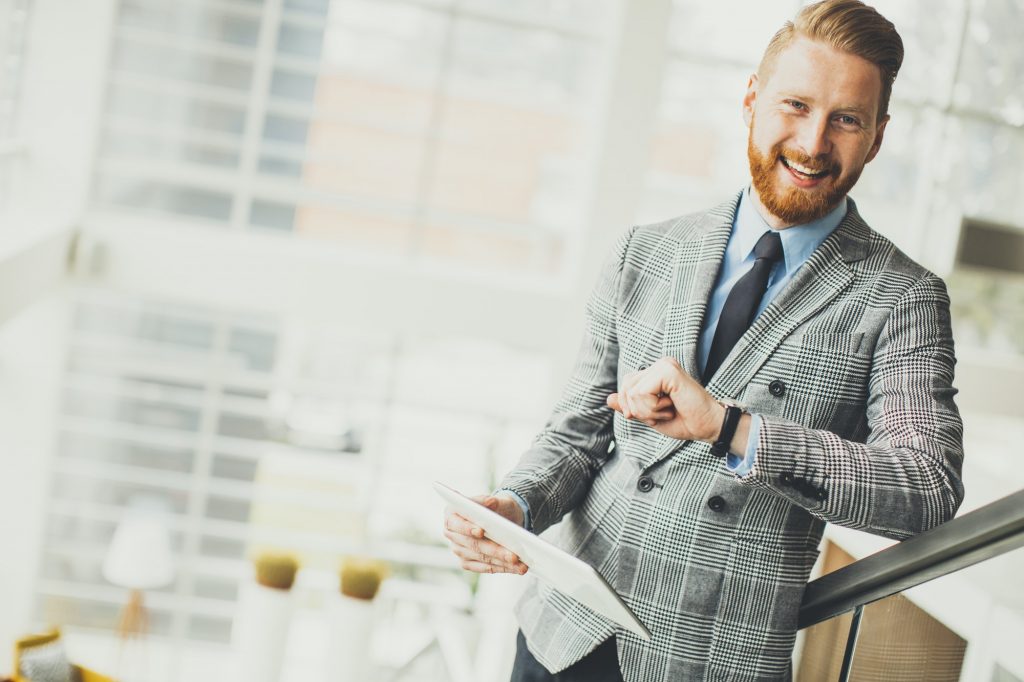 Young businessman using tablet and looking at his watch